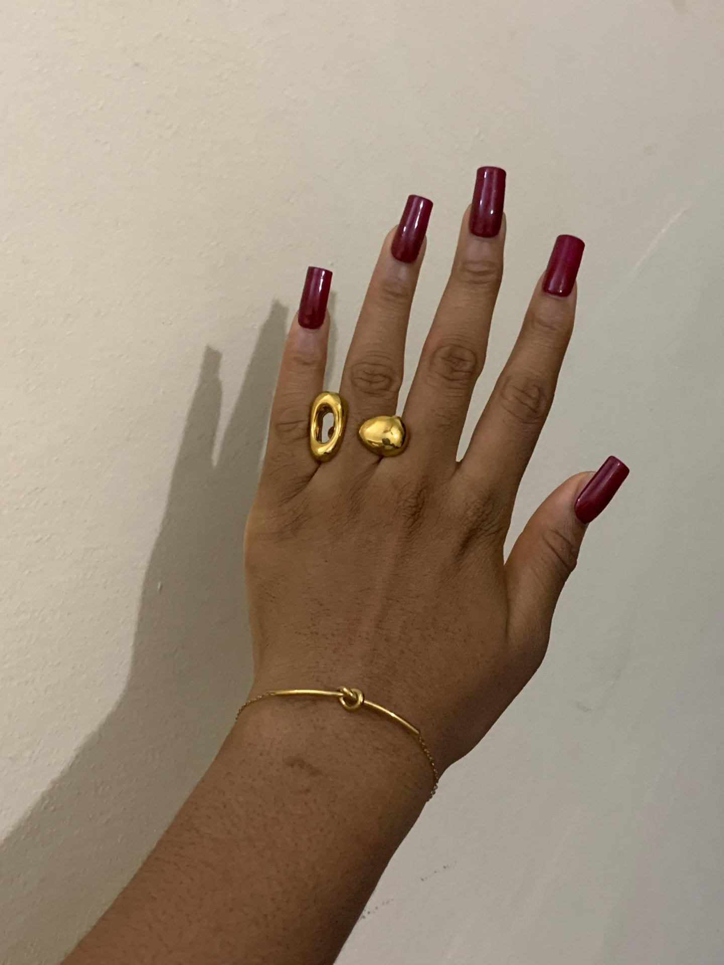 Two chunky gold rings and a knot bracelet worn on a hand